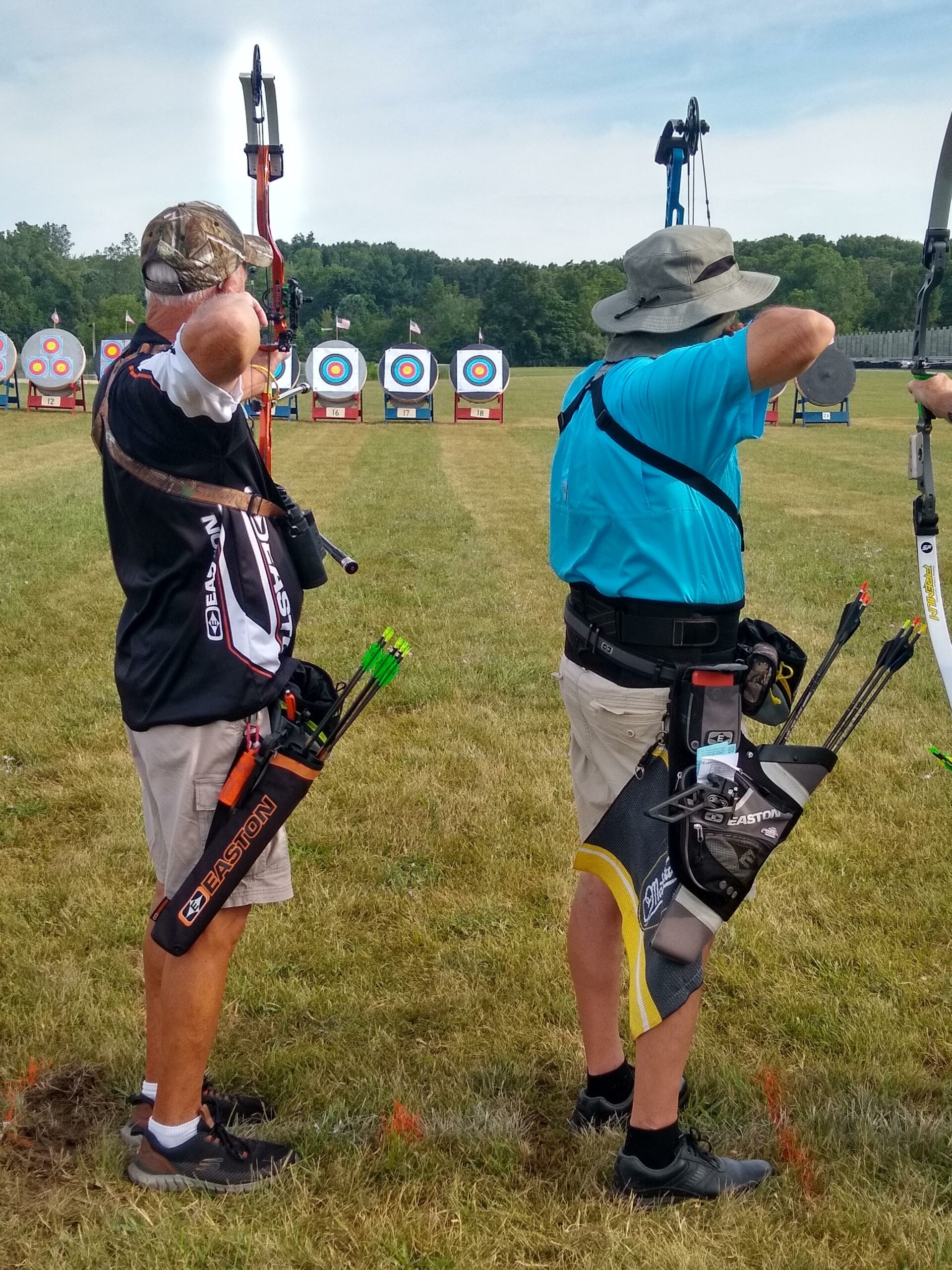 Two participants draw their bows back and aim to shoot the target.